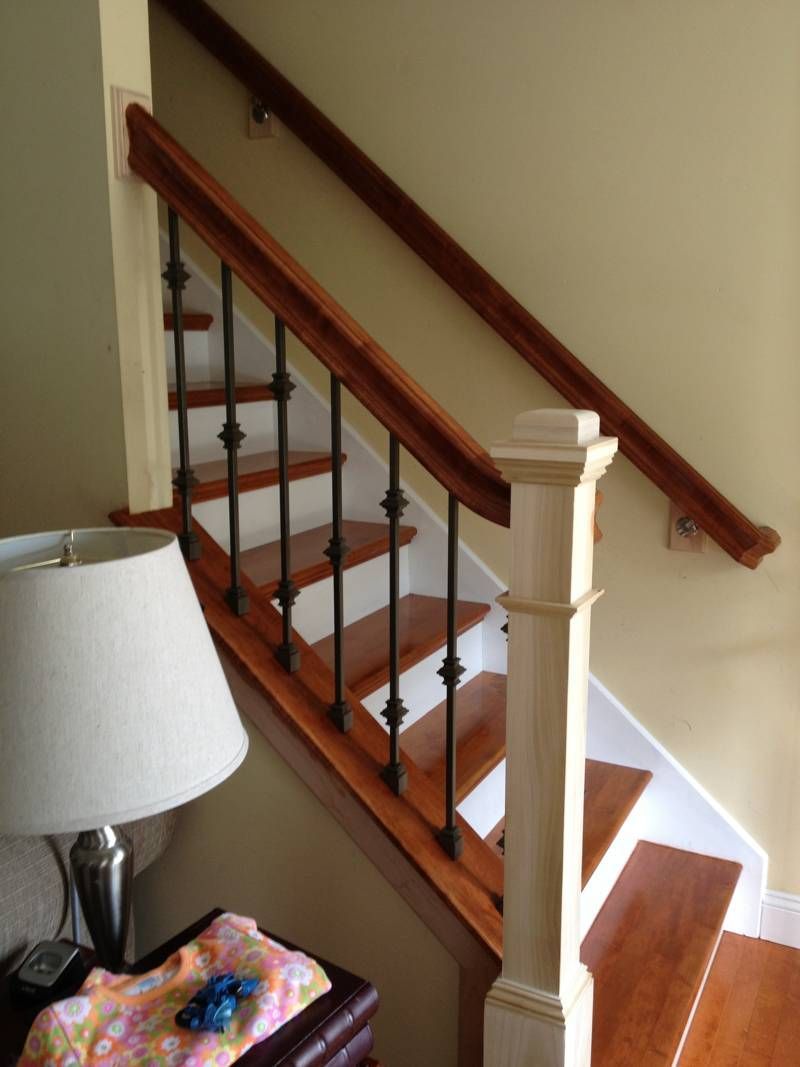 Wooden staircase with white risers, dark handrail, and cream walls beside a lamp-lit interior corner