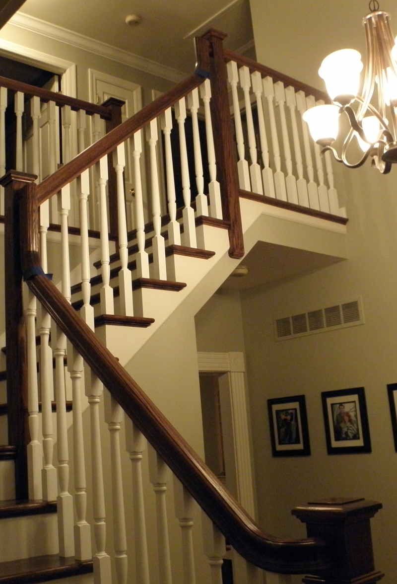 Elegant staircase with white balusters, dark wood railing, and chandelier in a warmly lit foyer