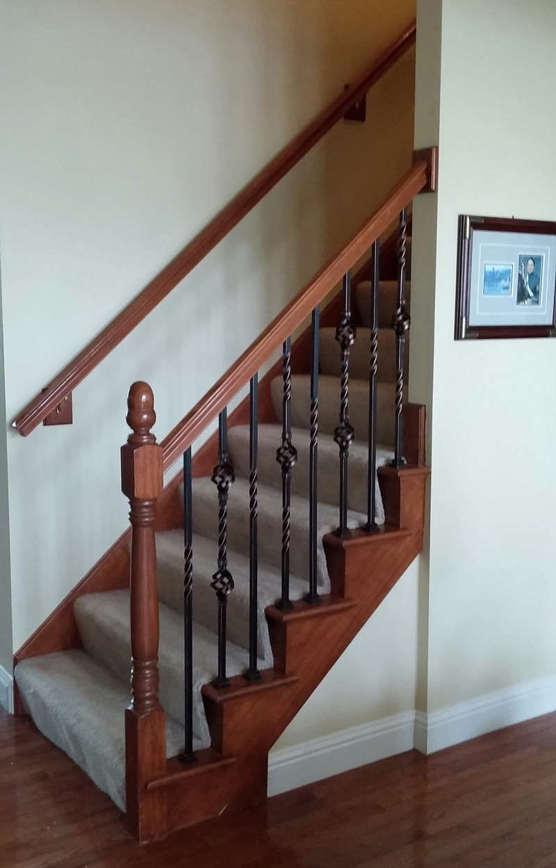 Wooden staircase with dark iron balusters in a white-walled interior room