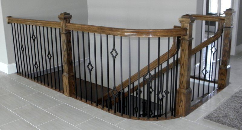 Wooden staircase railing with black metal balusters around a stairwell in a tiled interior.