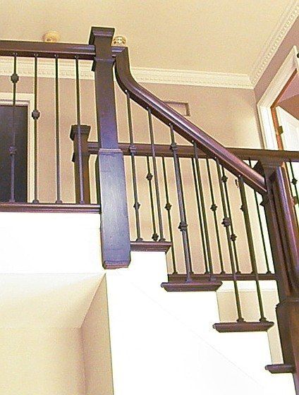 Staircase with dark wood handrail and black balusters in a beige interior.