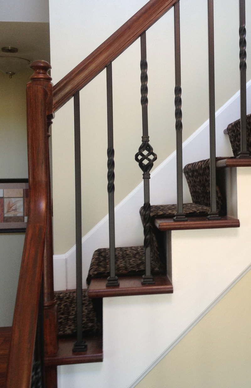 Indoor staircase with wooden handrail, dark balusters, and patterned carpeted steps.
