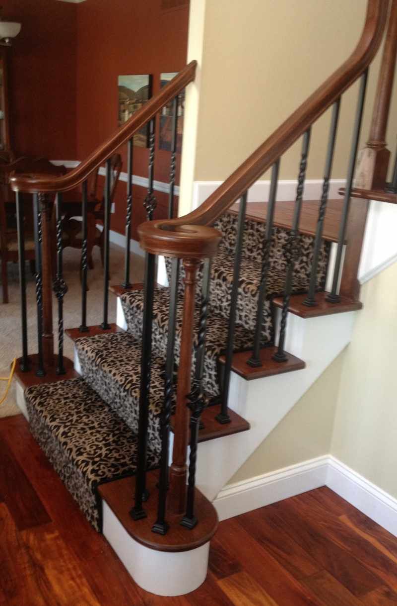 Carpeted staircase with wooden railings and black iron balusters in a home interior