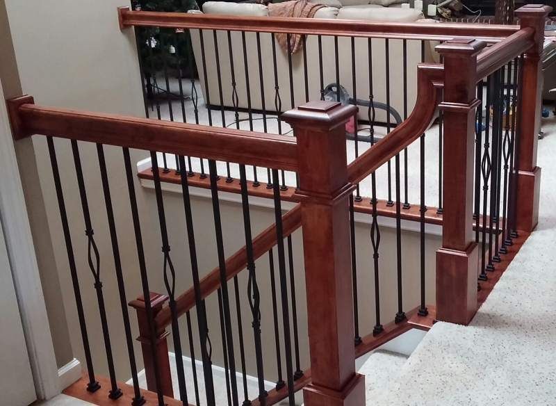 Wooden stair railing with dark metal balusters beside a carpeted hallway window.