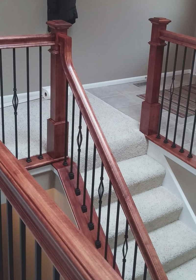 Carpeted staircase with wooden railings and black iron balusters in a home interior