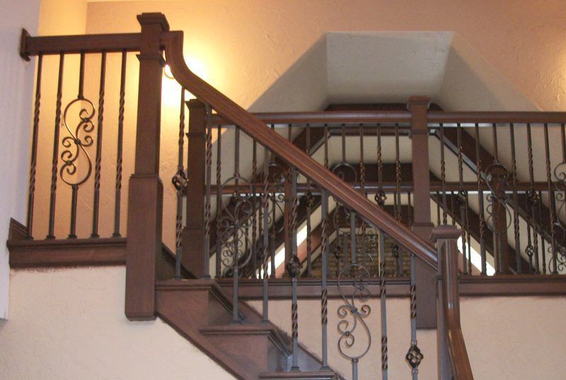 Indoor staircase with dark wood banister and decorative iron railing, viewed from a landing.