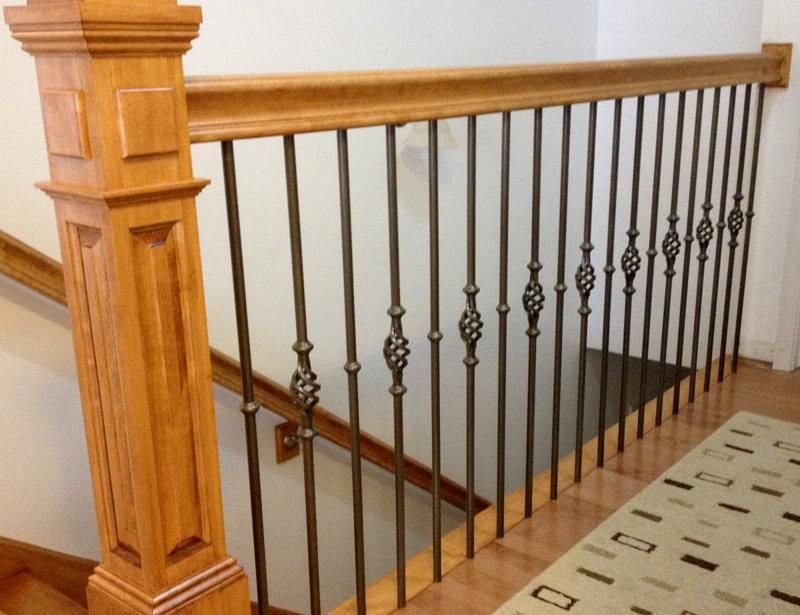Wooden staircase railing with black metal balusters beside a carpeted stairwell