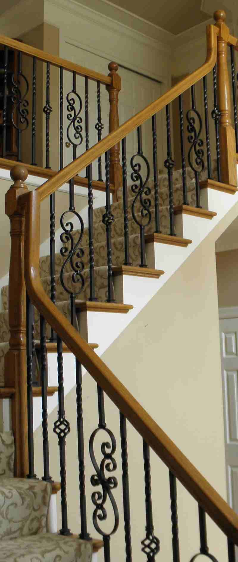 Wooden staircase with dark wrought-iron balusters and light carpeted steps in a home interior