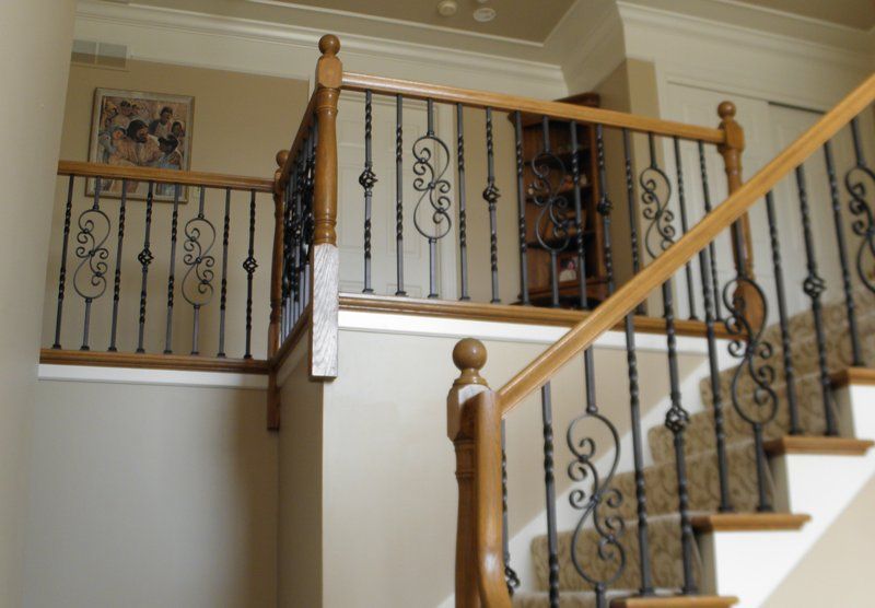 Staircase with beige walls and wooden railings, featuring black wrought-iron balusters and decorative scrollwork.