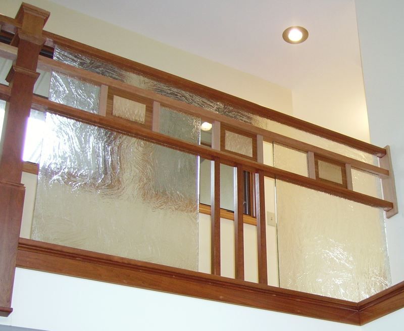 Wooden stair railing with frosted glass panels inside a bright interior hallway