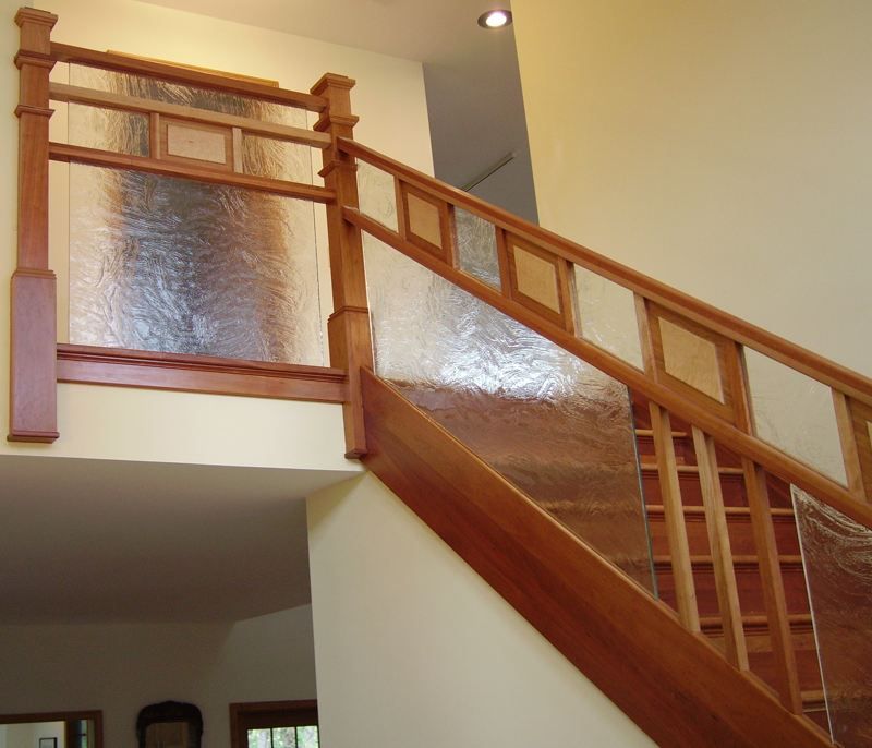Wooden staircase with varnished railing and textured glass panels in a warmly lit interior.