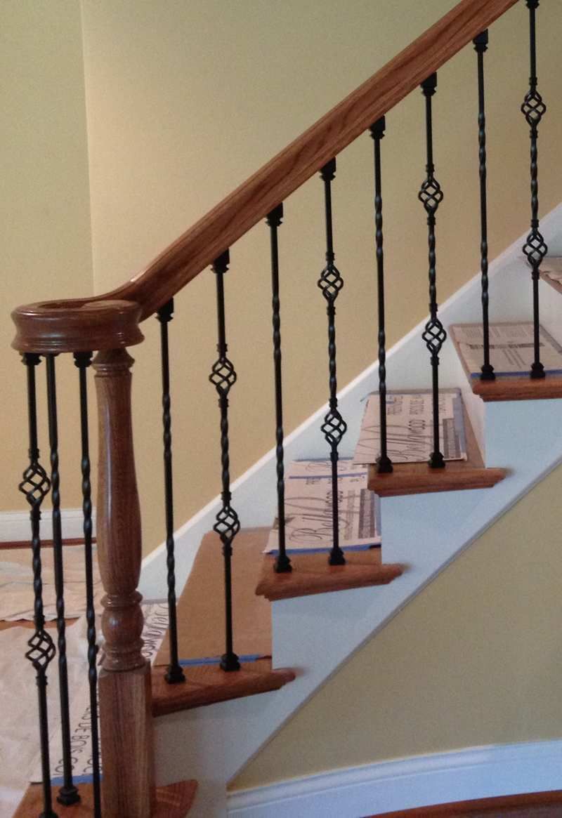 Indoor staircase with wooden handrail and black wrought-iron balusters on beige walls
