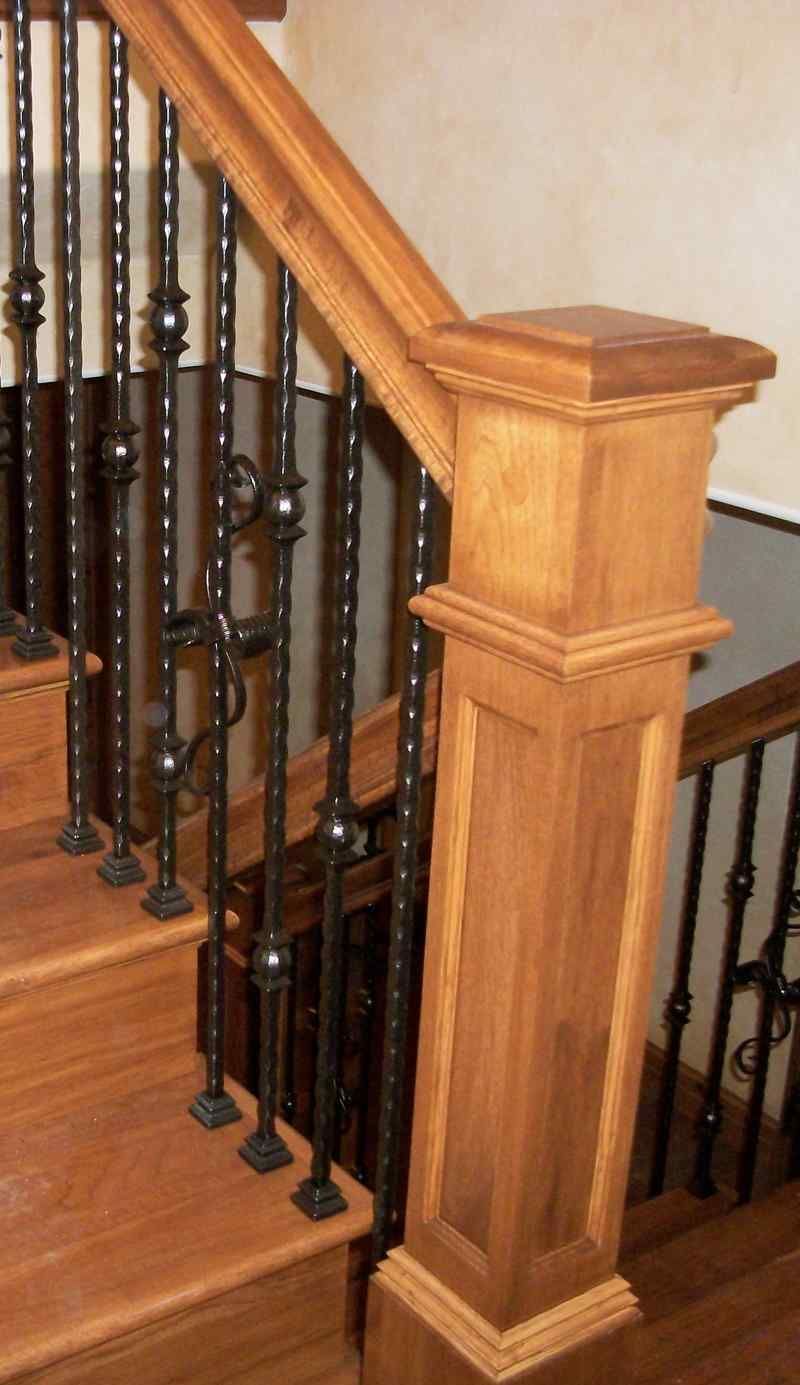 Wooden staircase railing with dark metal balusters and a square newel post