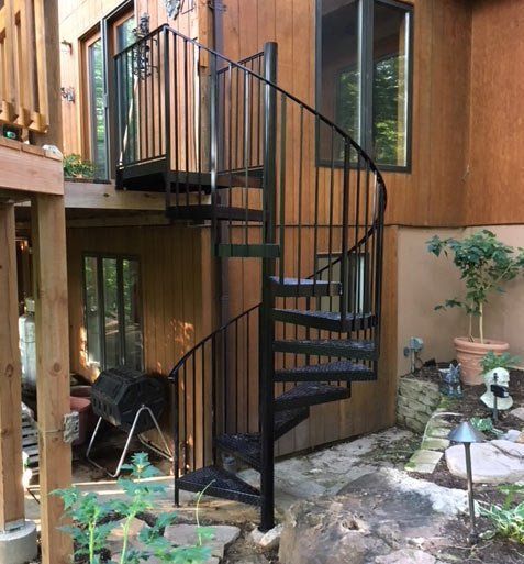 Spiral staircase beside a wooden house deck in a small outdoor courtyard with stone paving and plants