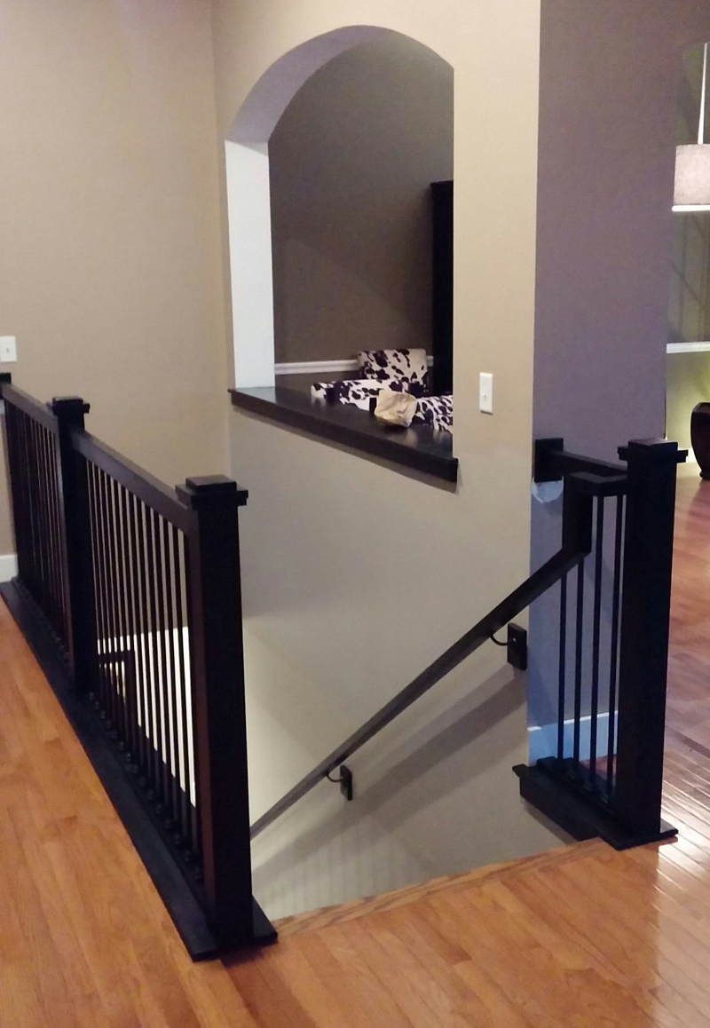 Staircase landing with black railings, gray walls, and an arched opening overlooking a lower level.