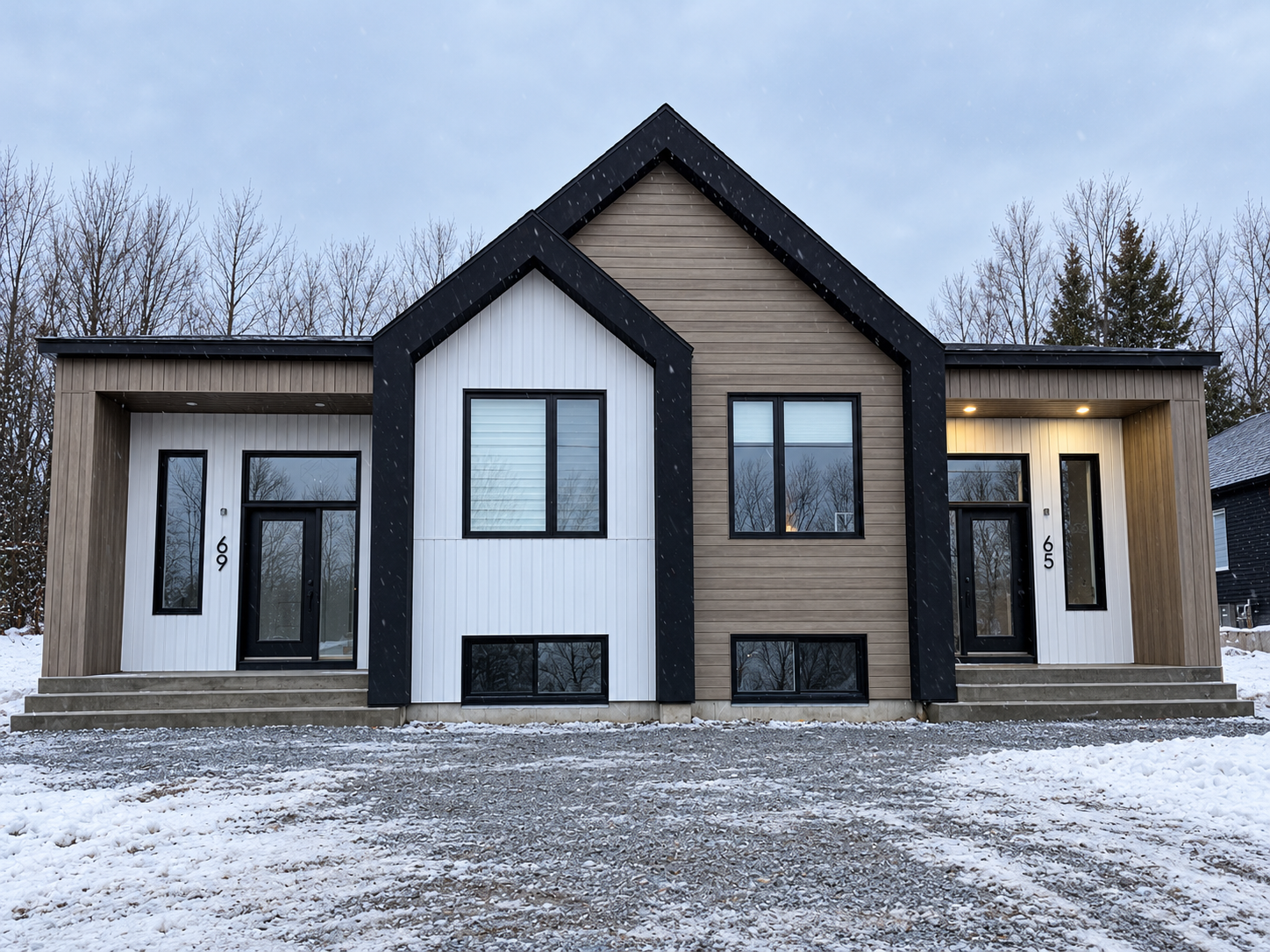 Maison moderne beige et noire, avec de la neige au sol et des arbres dénudés à l’avant