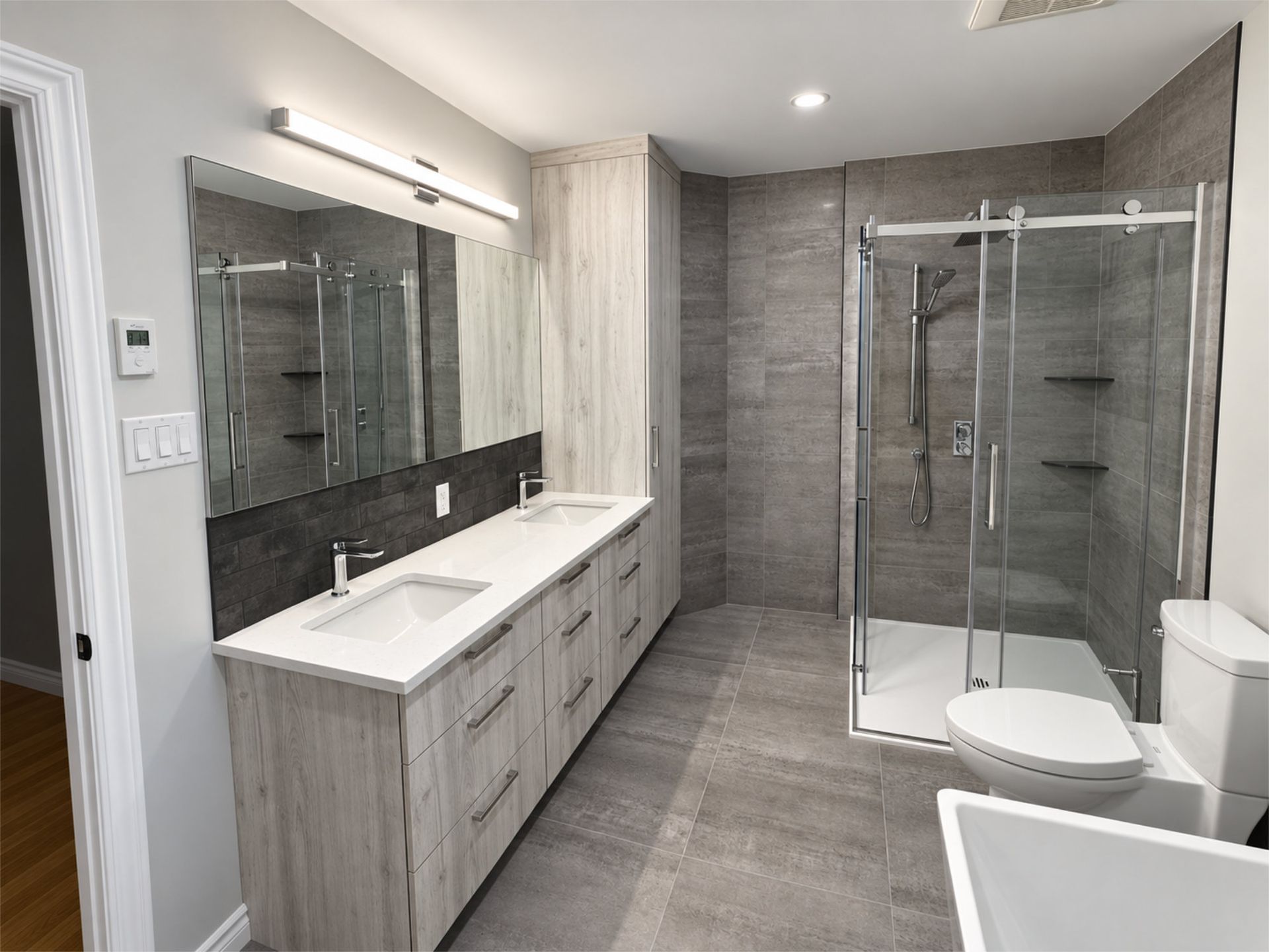 Salle de bains moderne aux tons gris, avec double vasque, grand miroir et douche à paroi vitrée.
