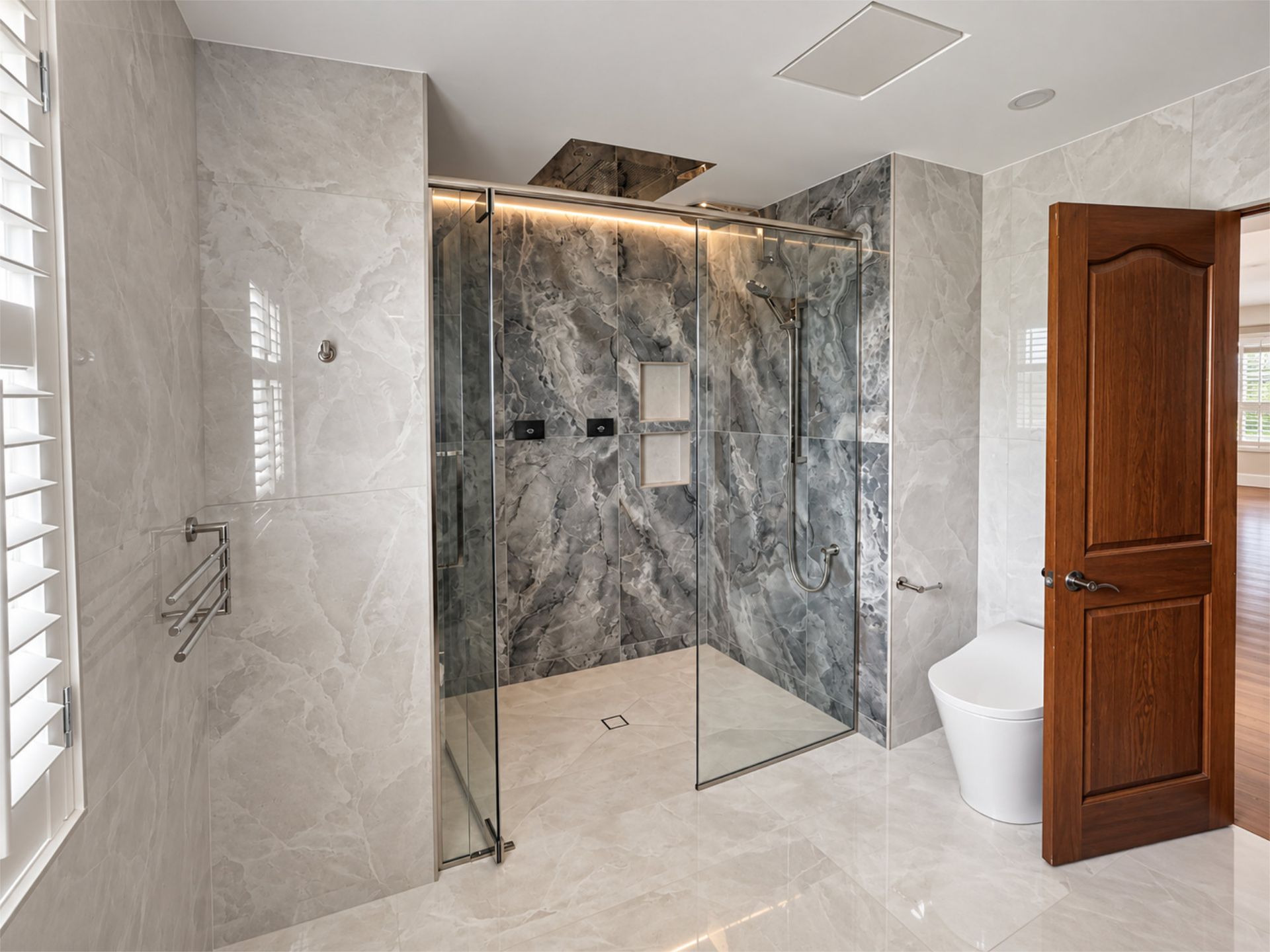 Salle de bains moderne avec douche à l’italienne en verre, carrelage en marbre gris et porte en bois.