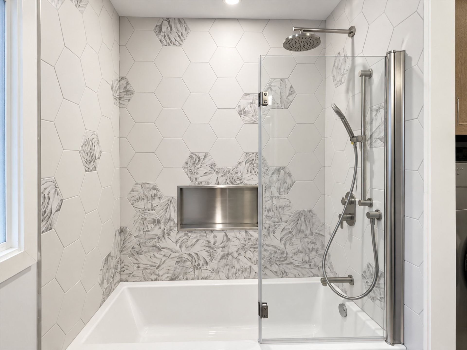 Salle de bains moderne blanche avec carrelage hexagonal, touches florales sur les murs et baignoire-douche avec paroi vitrée