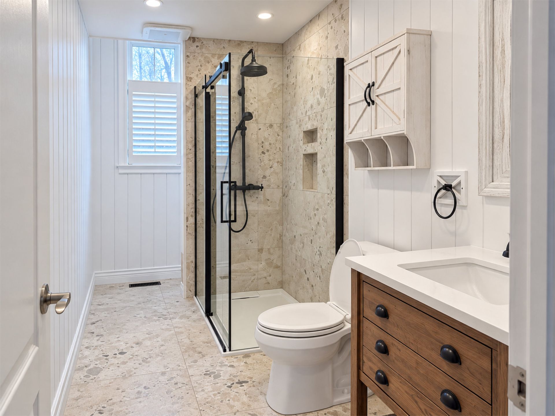 Salle de bains lumineuse avec douche à l’italienne, toilettes, meuble-vasque et sol en carrelage clair moucheté.