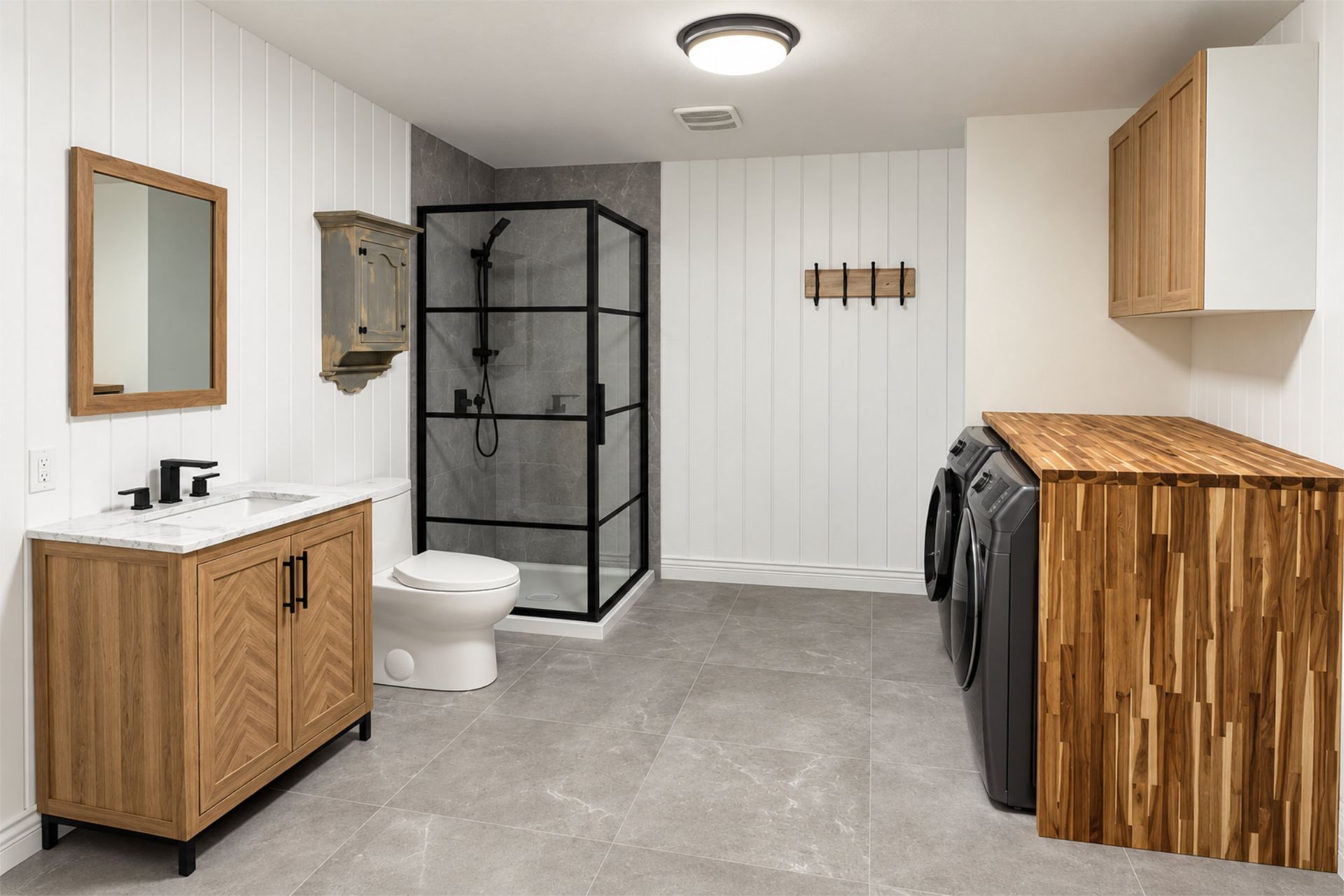 Buanderie avec cabine de douche noire, meubles en bois, lavabo, toilettes et lave-linge séchant sur un sol carrelé gris