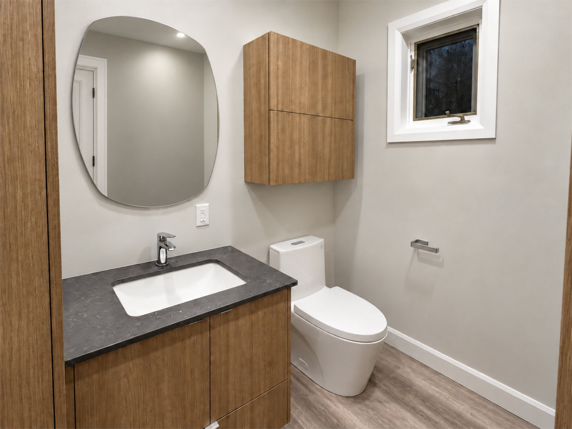 Salle de bains moderne avec meuble vasque, miroir rond, toilettes, meuble en bois et petite fenêtre
