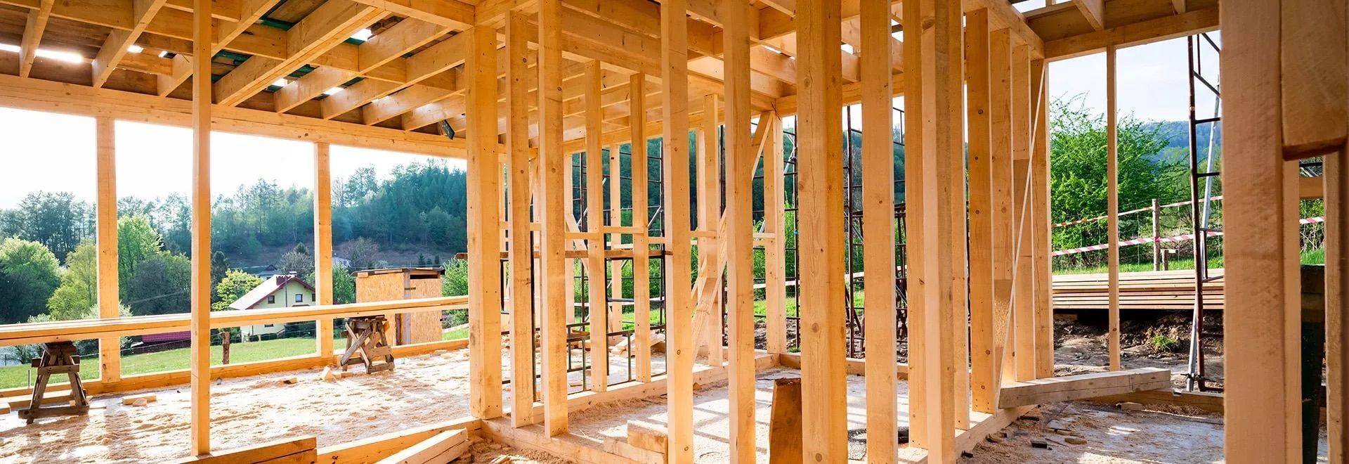Maison à ossature bois en construction, avec des poutres apparentes, une charpente de toit et des fenêtres donnant sur un paysage verdoyant