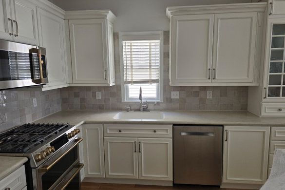 Bright white kitchen with stainless steel appliances, beige tile backsplash, and a window over the sink.