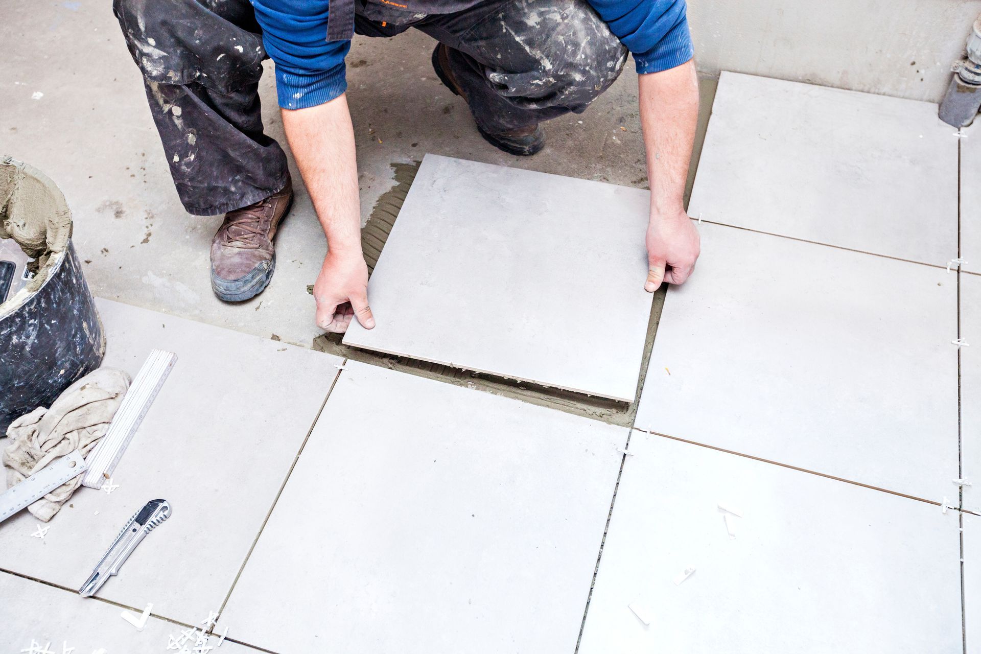Worker installing large white floor tiles with spacers in a room