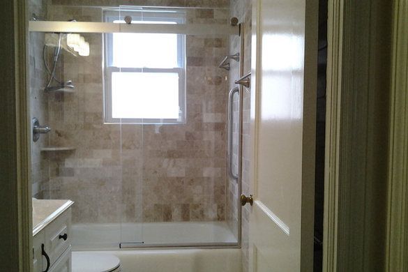Small bathroom with a glass-enclosed shower, bathtub, window, and vanity.