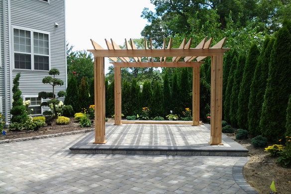 Wooden pergola on a stone patio in a landscaped backyard beside a house