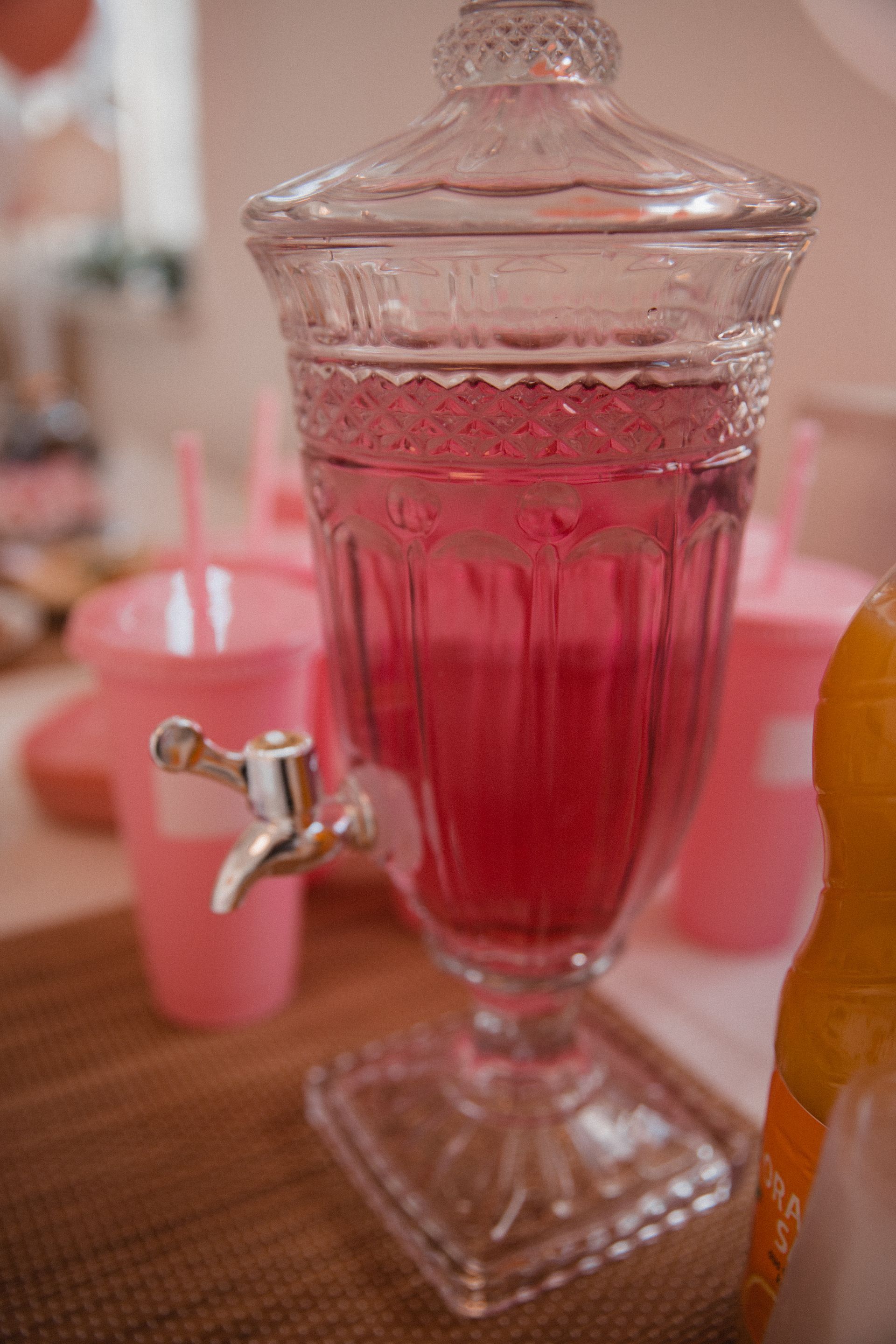 Auf einem Tisch steht ein mit einer rosa Flüssigkeit gefüllter Glasspender.