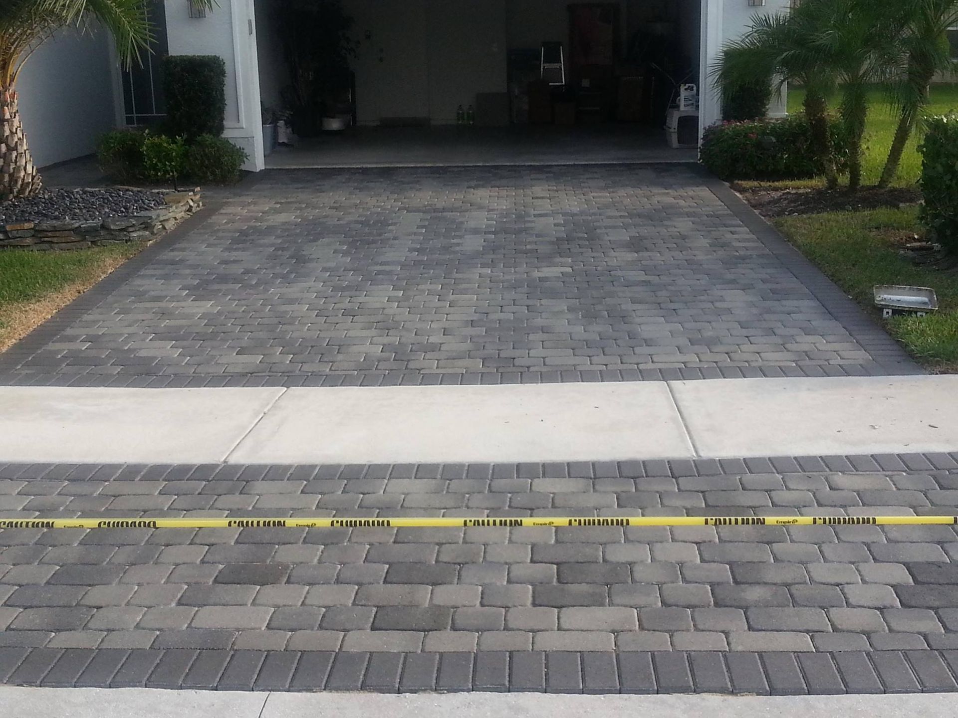 A brick driveway leading to a garage with a yellow tape on the sidewalk