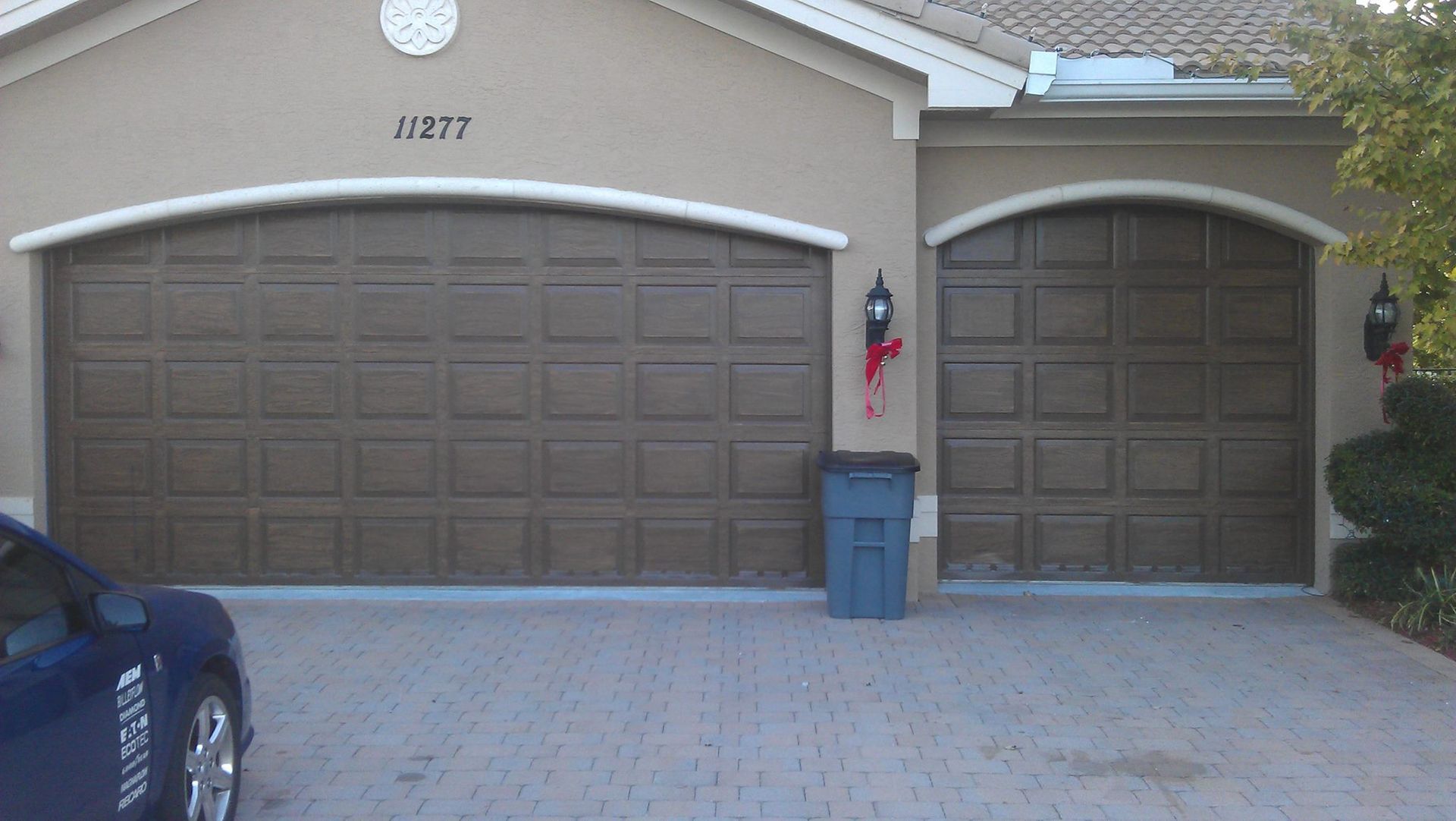 A car is parked in front of a house with two garage doors.