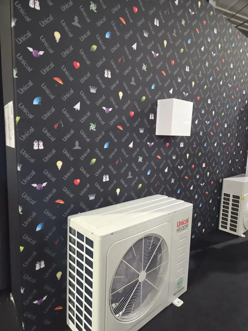 Condizionatore d'aria bianco a parete, installato su una parete decorata, in una stanza con pavimento nero e una seconda unità sullo sfondo.