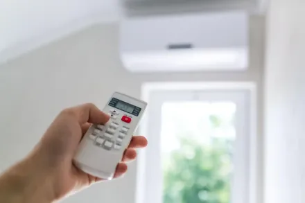 Mano che impugna un telecomando puntato verso un condizionatore d'aria a parete in una stanza luminosa