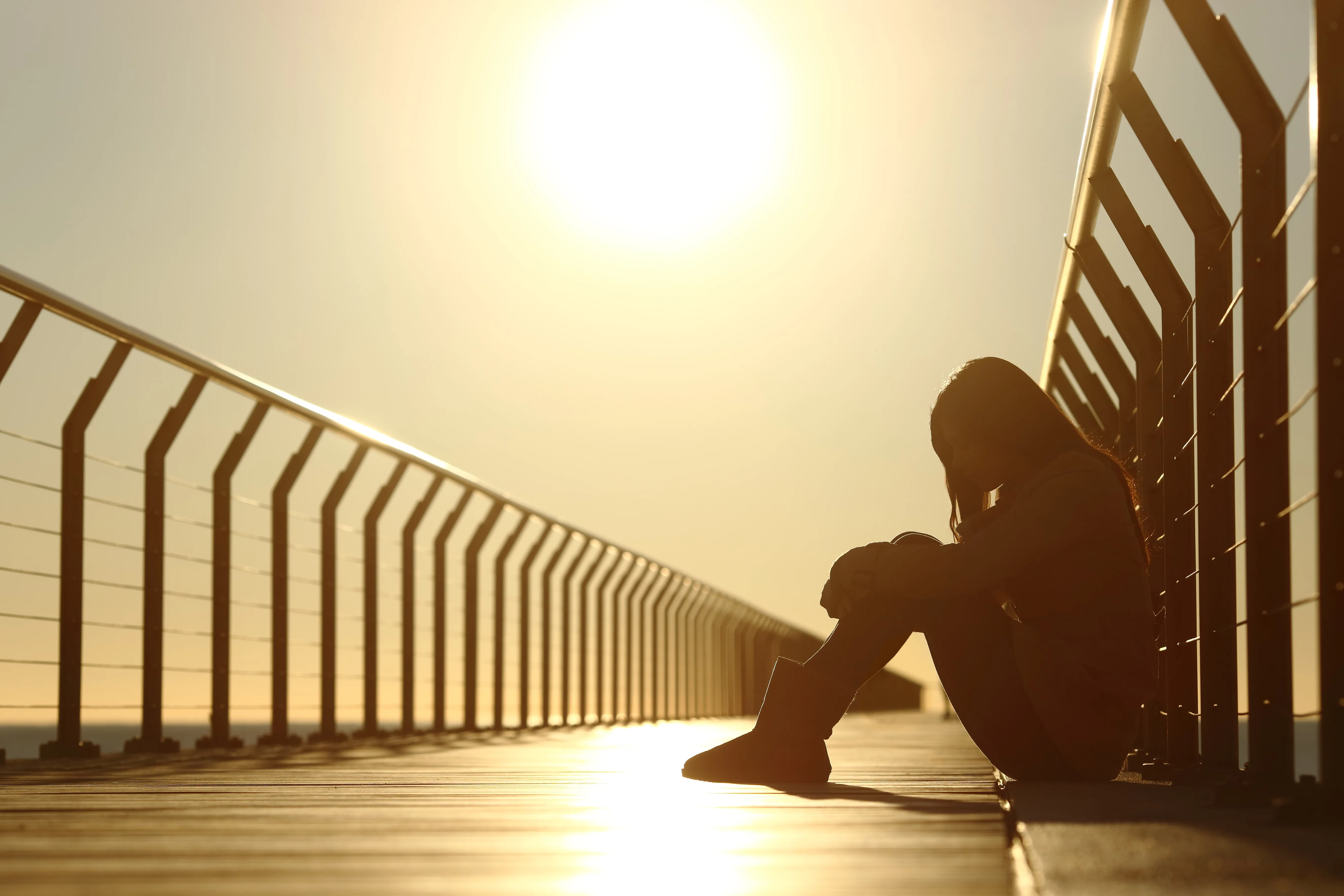 A teenage girl sitting on a bridge feeling sad.