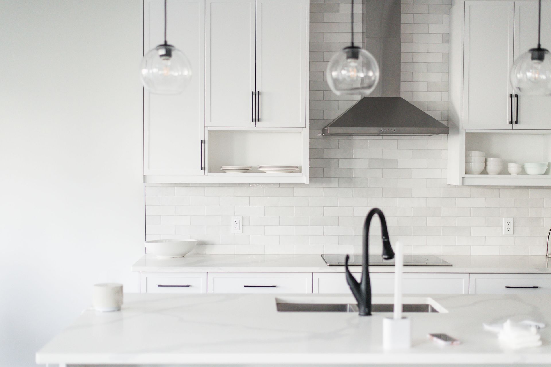 Modern white kitchen with black faucet, range hood, and hanging lights.