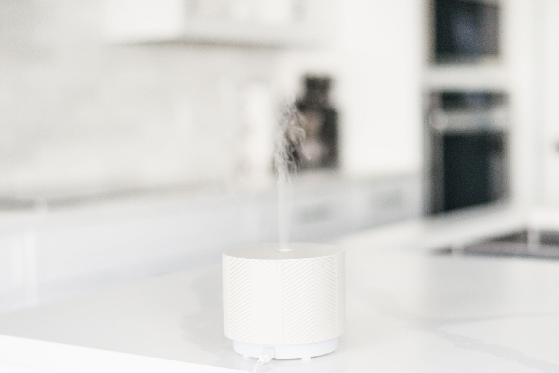 White essential oil diffuser with steam on a white countertop in a kitchen.