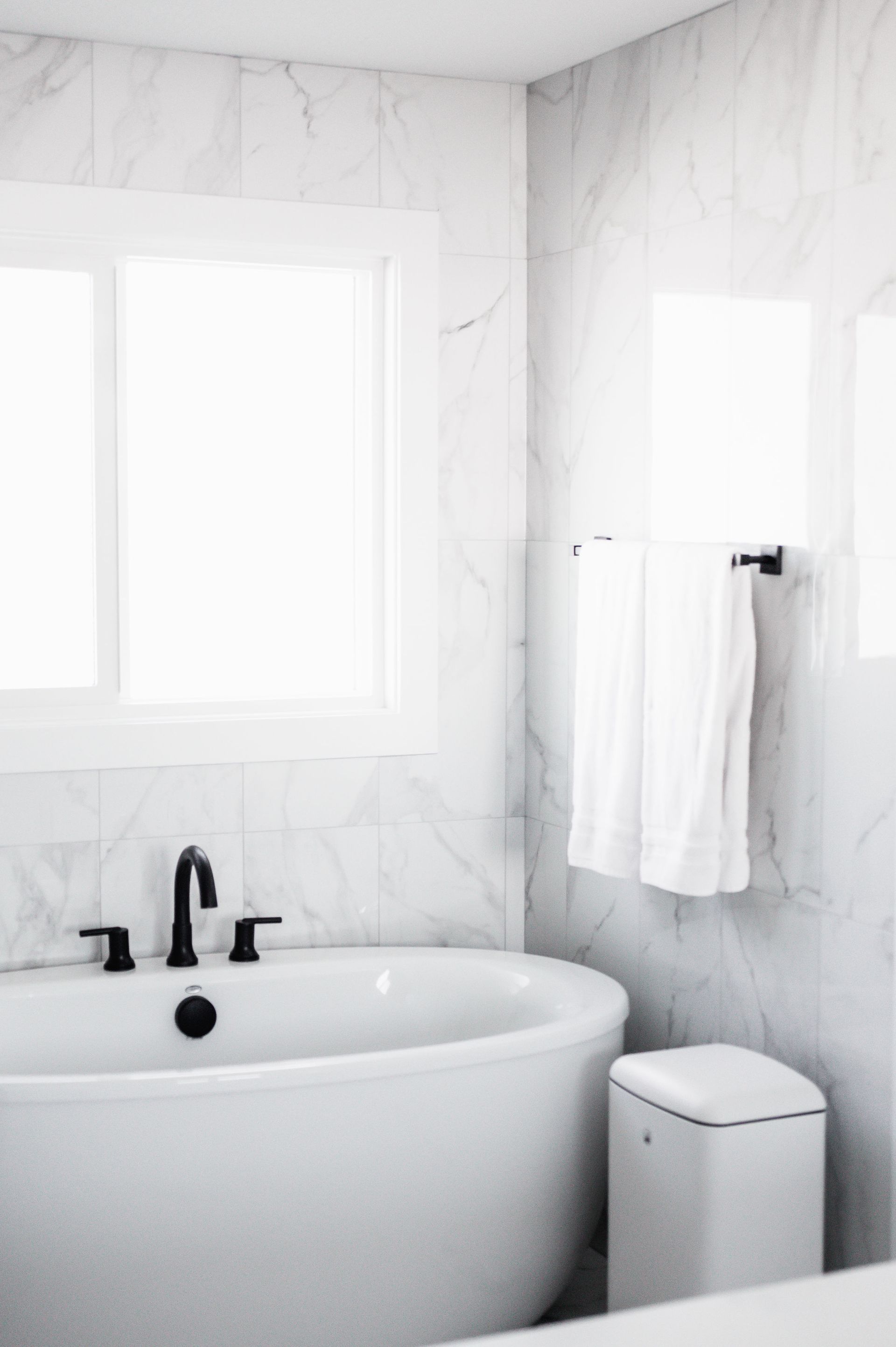 White bathroom with a tub, window, and towel rack.