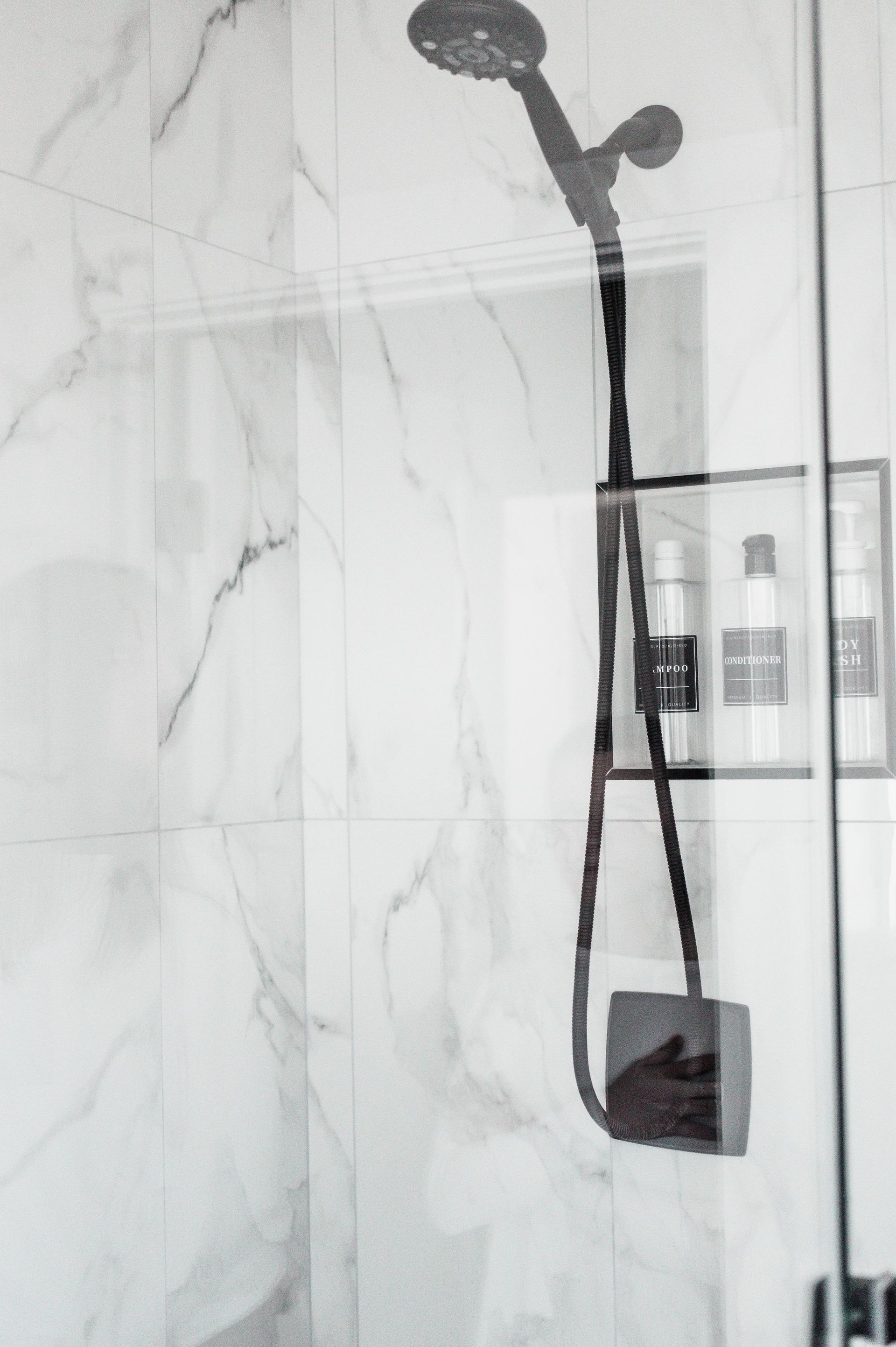 Shower with marble-look tile and a black showerhead.