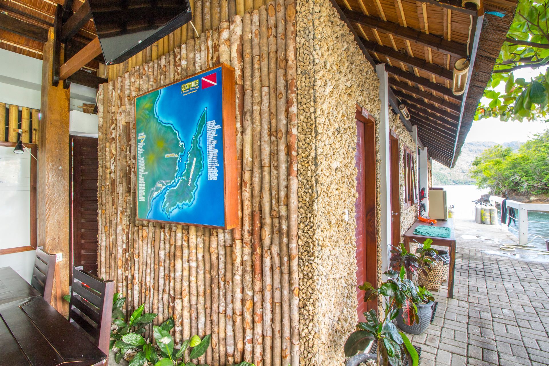 Wooden resort walkway with a blue island map sign and potted plants under a thatched roof