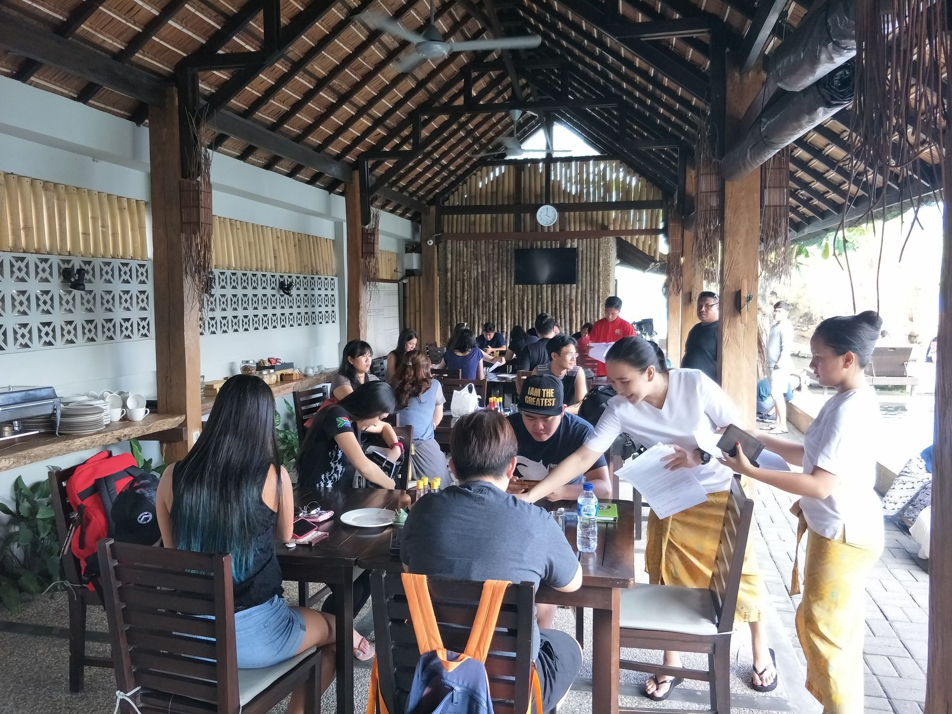 Group seated around tables in a rustic open-air pavilion, studying and writing together