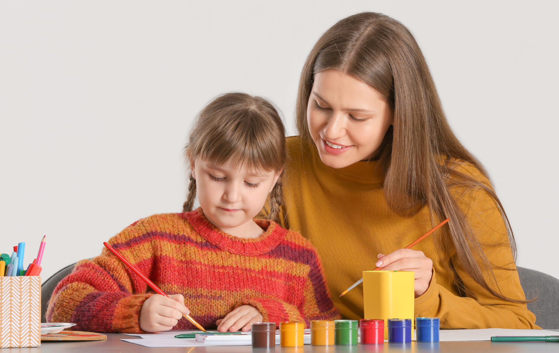 A woman and a little girl are sitting at a table painting.
