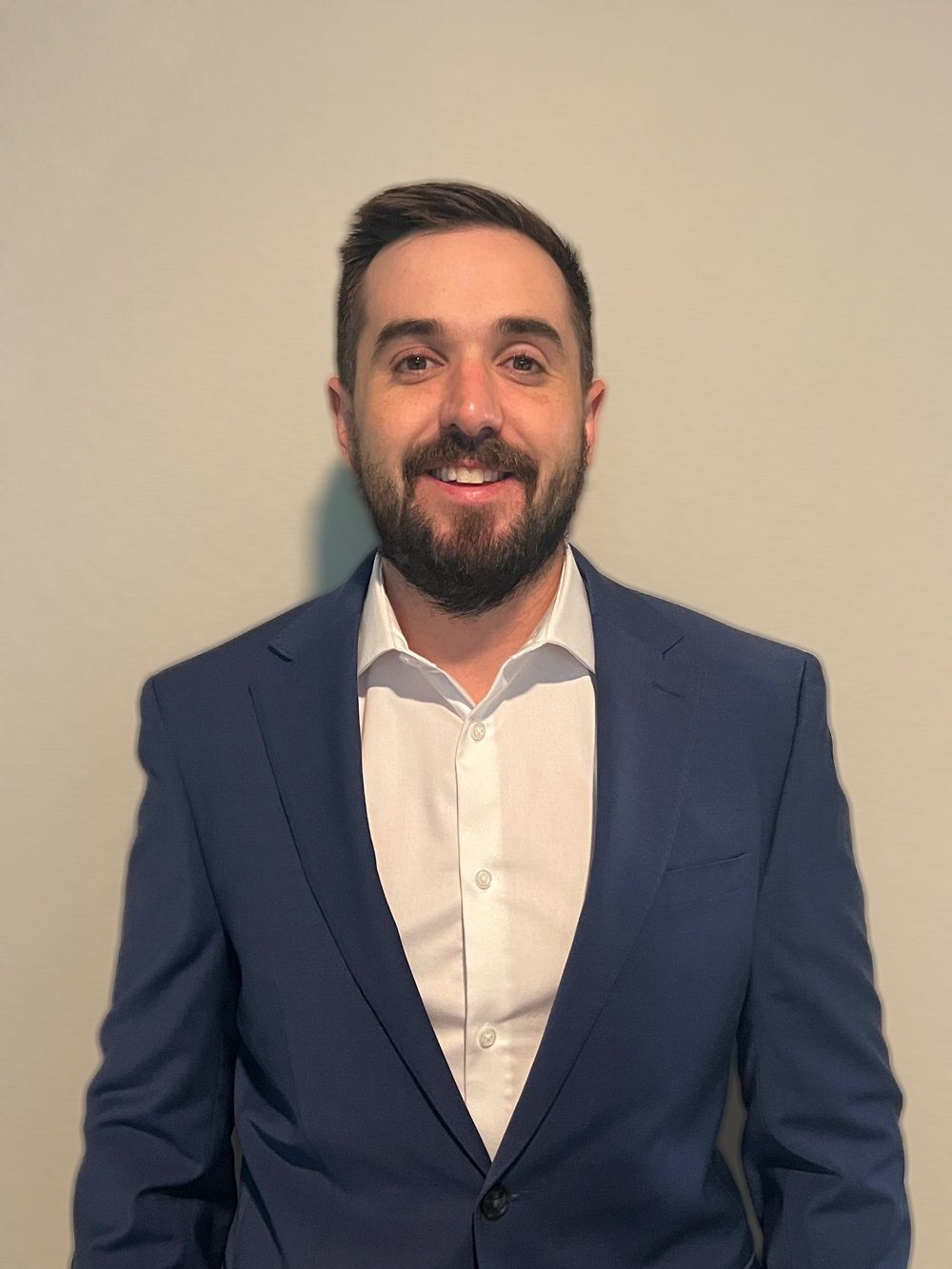 A man with a beard is wearing a blue suit and white shirt.