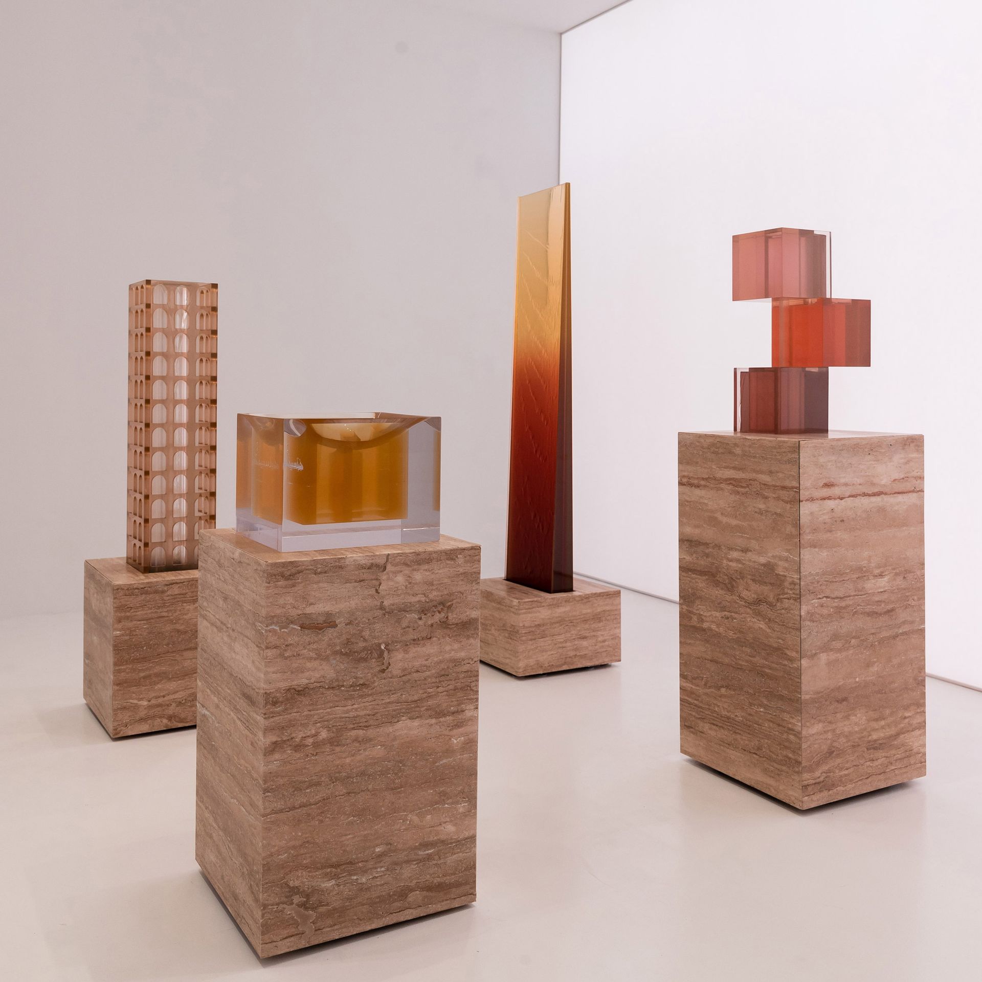 Vier sculpturen op stenen sokkels in een witte ruimte. Kleuren: glas, bruin en roodoranje.