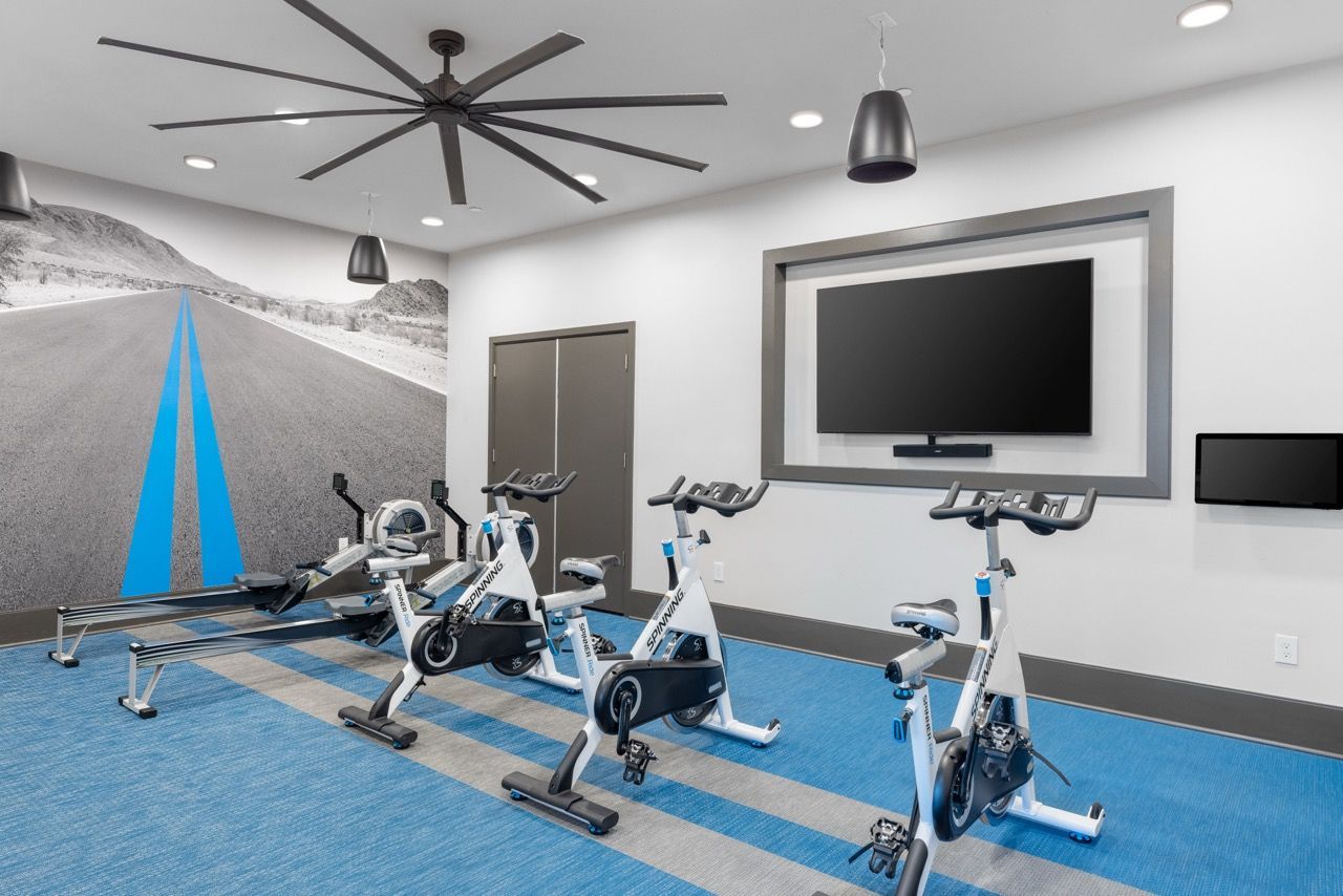Indoor fitness center with multiple stationary bikes, a rowing machine, and a wall-mounted TV.
