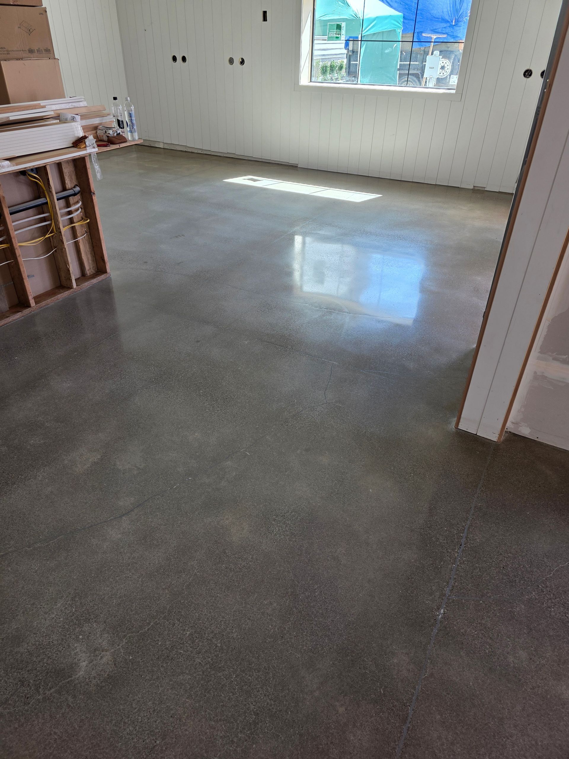 Empty room with gray concrete floor, white walls, and sunlight through a window.