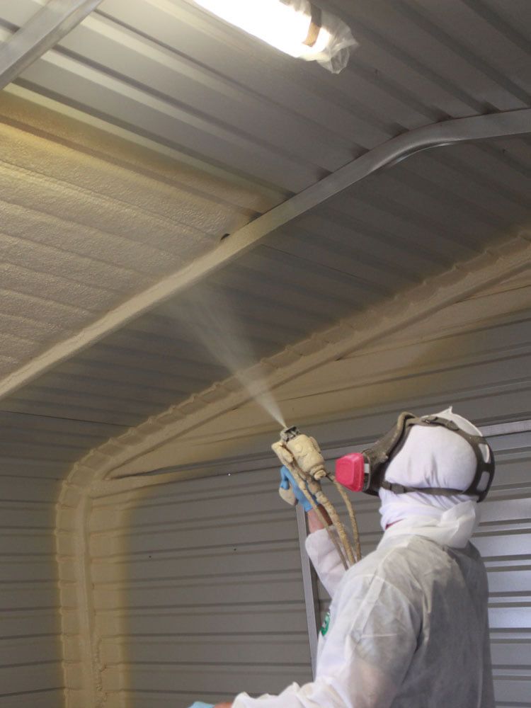 A man is spraying foam on the ceiling of a building.