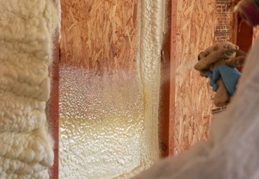 A person is spraying foam on a wooden wall.